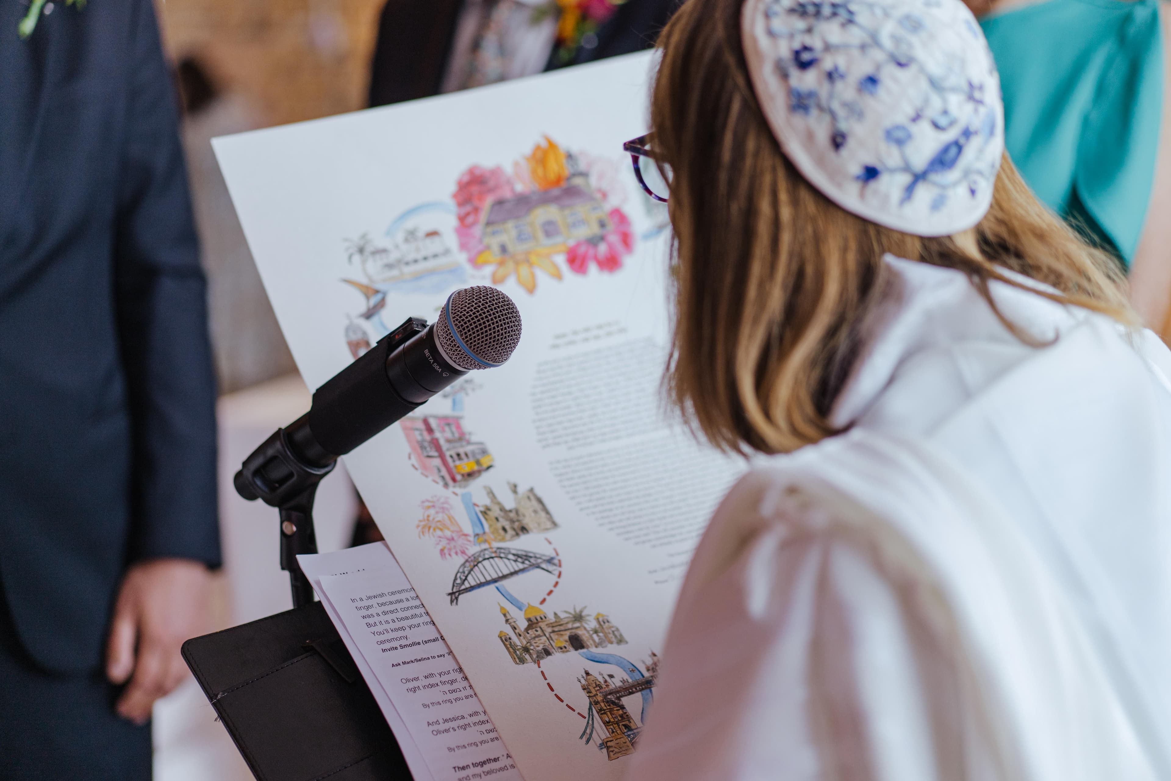 A personalised illustrated ketubah being read aloud at a Jewish wedding ceremony