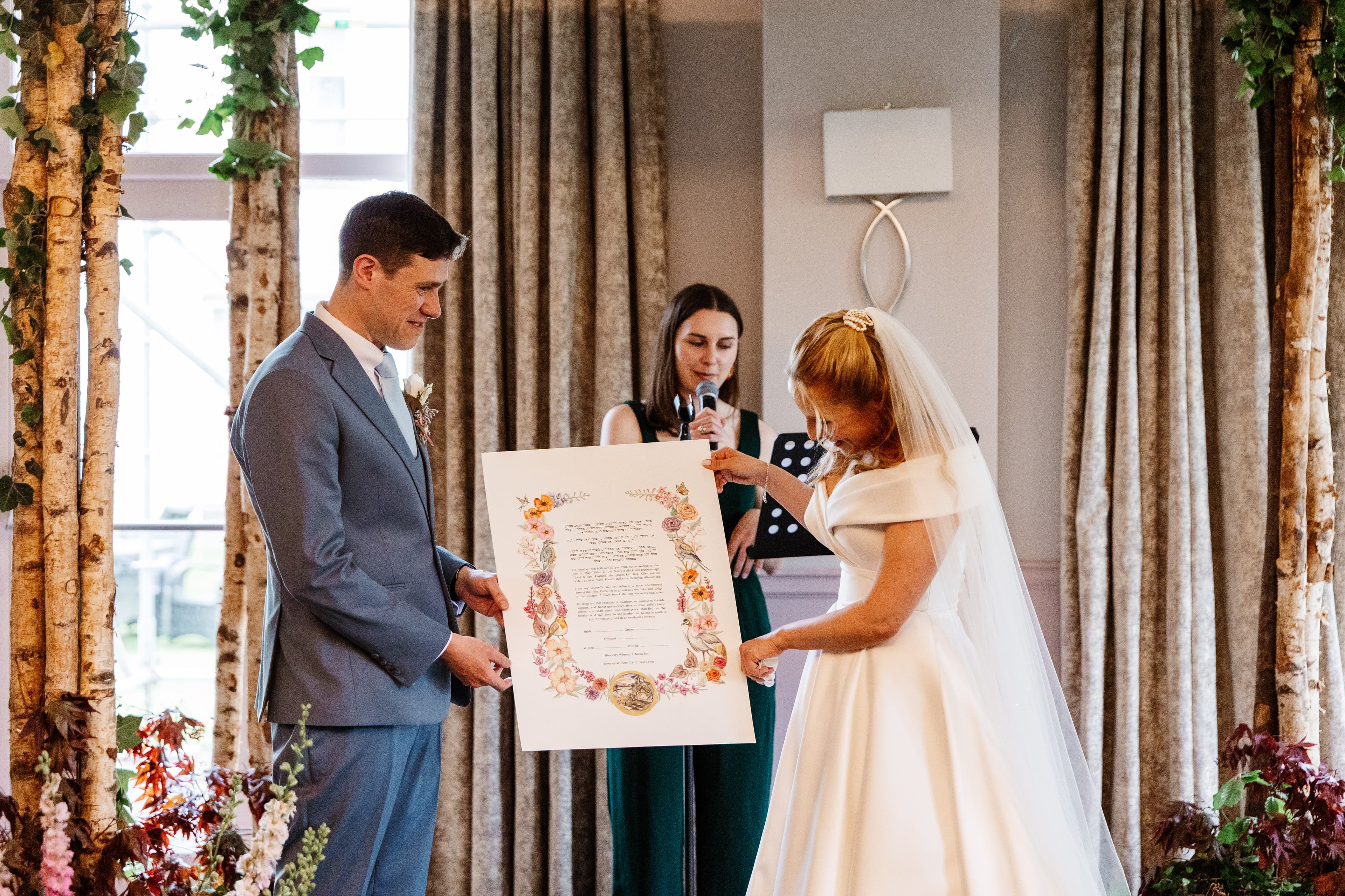 A newly married couple holding their personalised floral ketubah during their Jewish wedding ceremony